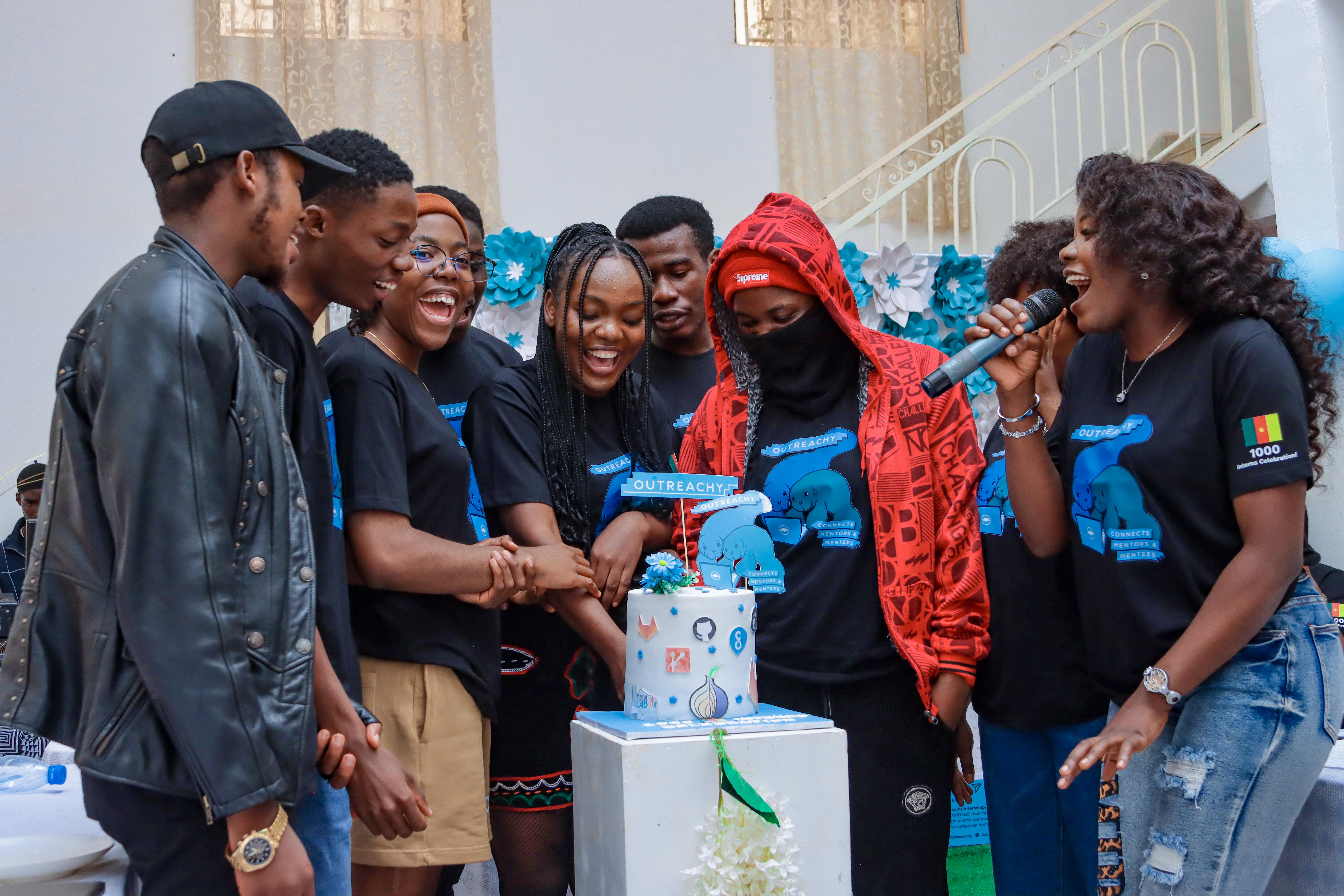 Group photo of Cameroon Outreachy interns cutting a cake with the Outreachy logo